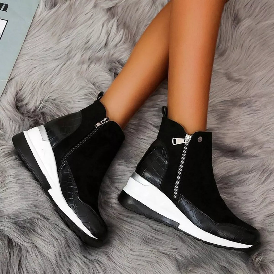 Black platform wedge boots with a white sole and side zipper, worn on a rug
