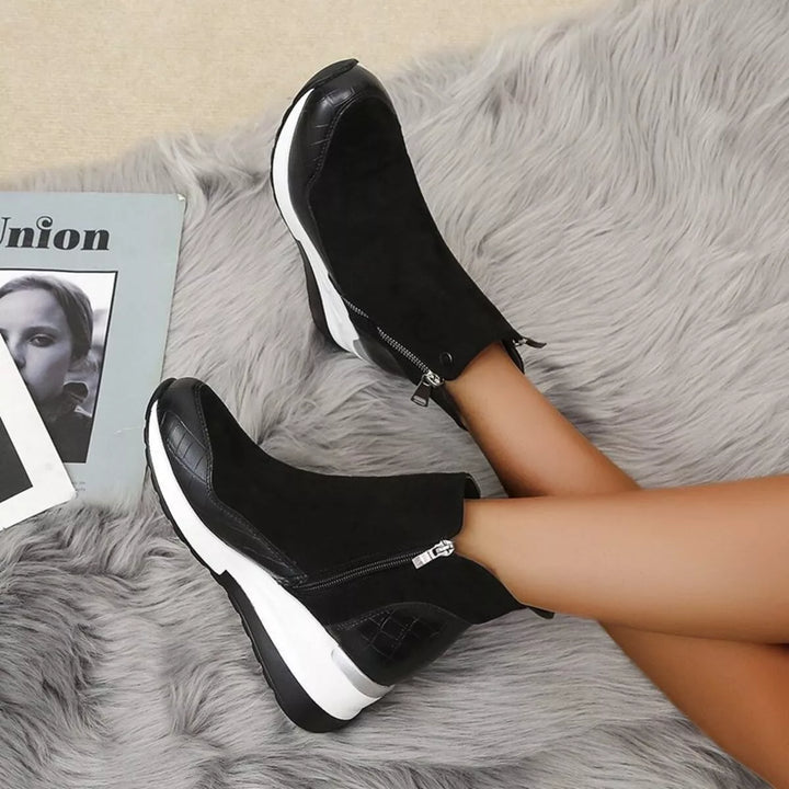 Black wedge platform ankle boots worn with legs crossed, showing the side zip