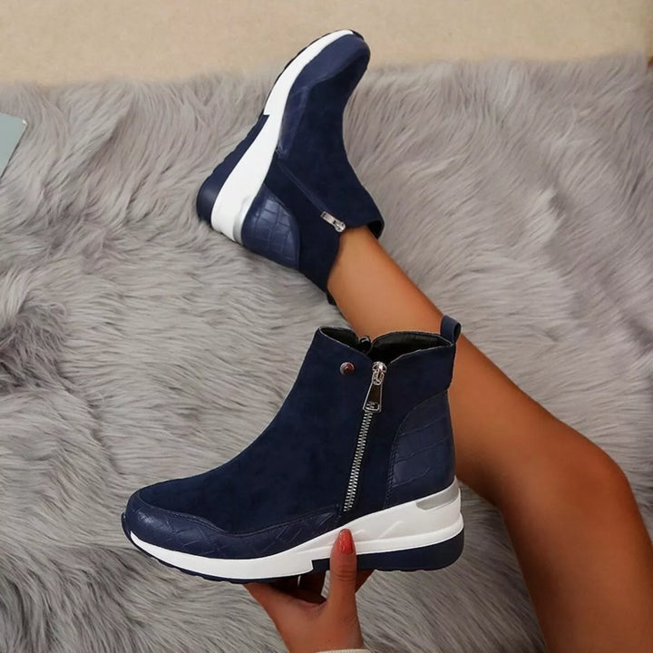 Navy wedge ankle boot held up to show the zipper and white sole