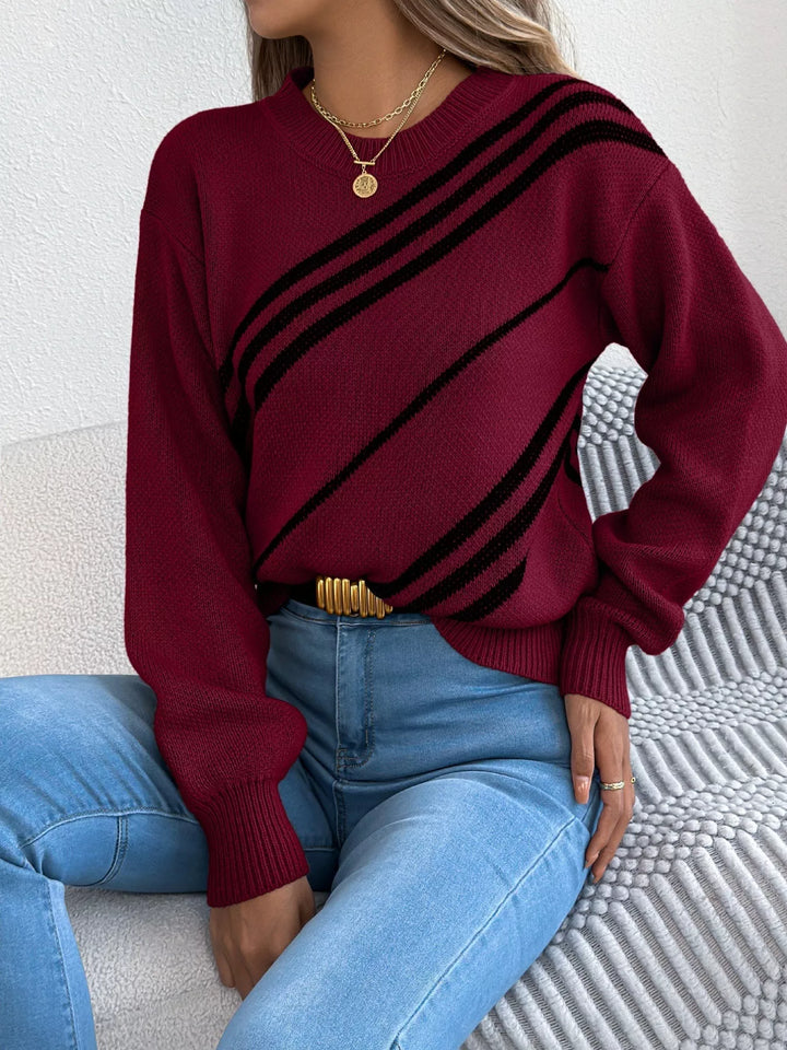 Burgundy striped sweater seated against a sofa arm, hand on hip