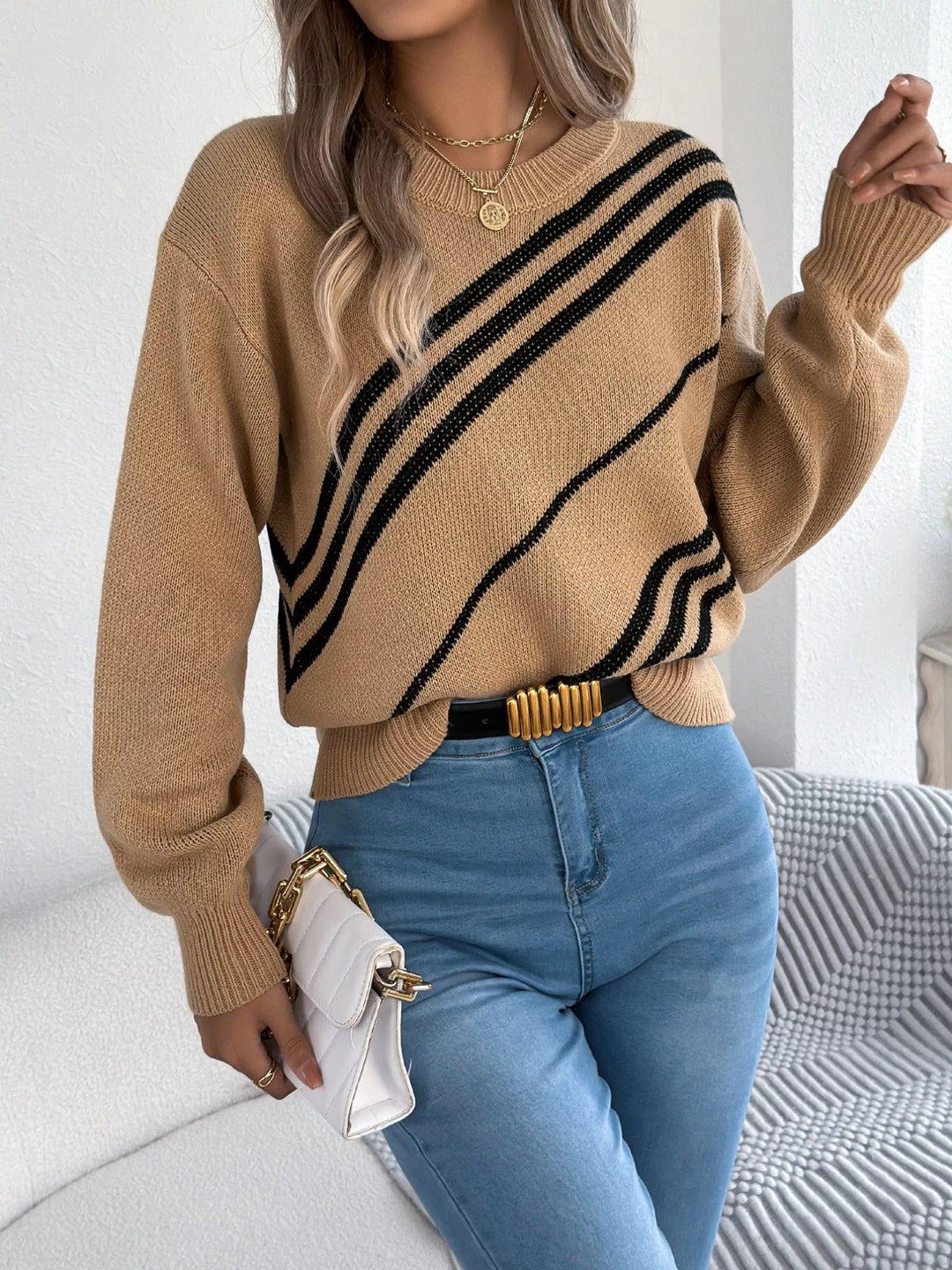 Women's camel fall sweater, crew neck with bold diagonal stripes, holding a white clutch