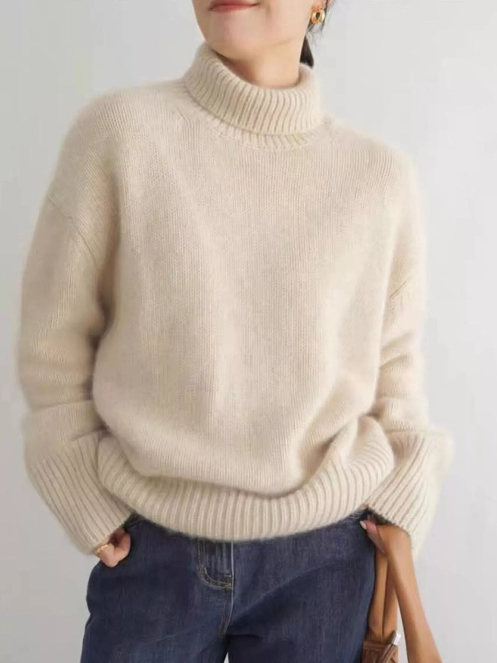 Cream turtleneck sweater with dropped shoulders, hands in pockets
