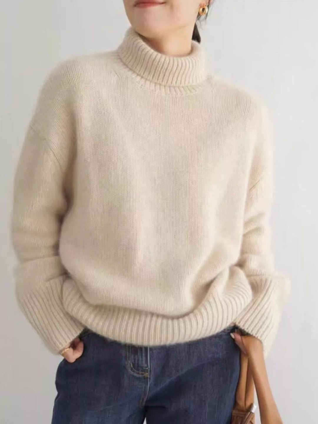Cream turtleneck sweater with dropped shoulders, hands in pockets