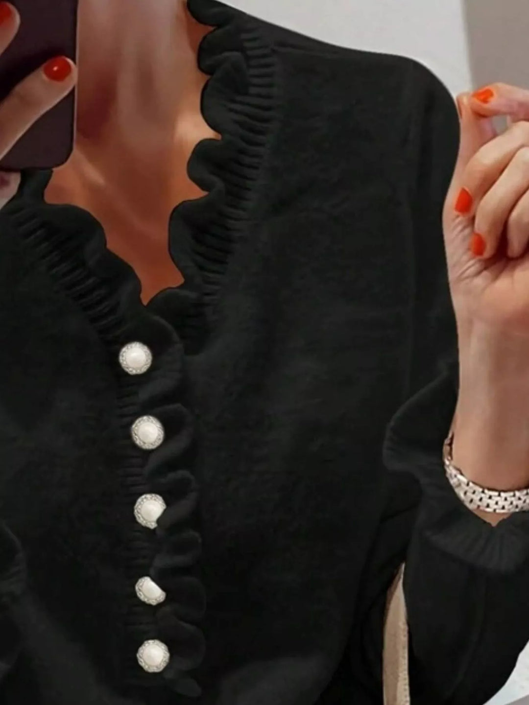 Close-up of the black sweater ruffled neckline and pearl look buttons
