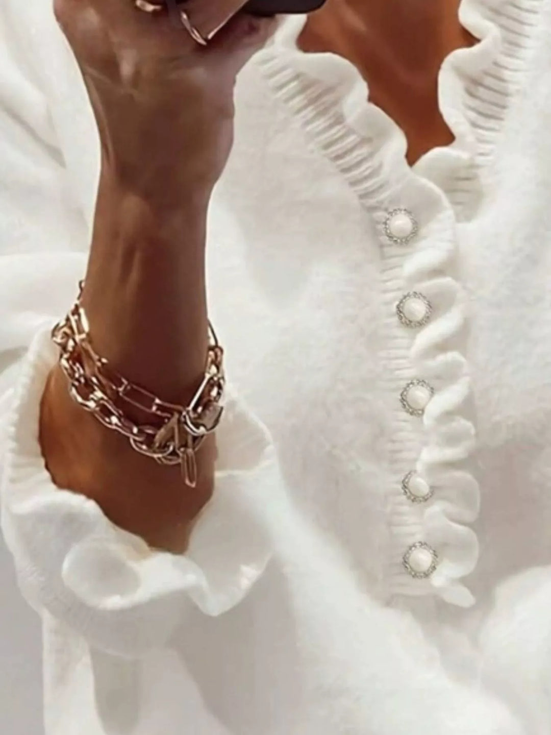 Close-up of the white sweater ruffle trim, buttons and ruffled cuff