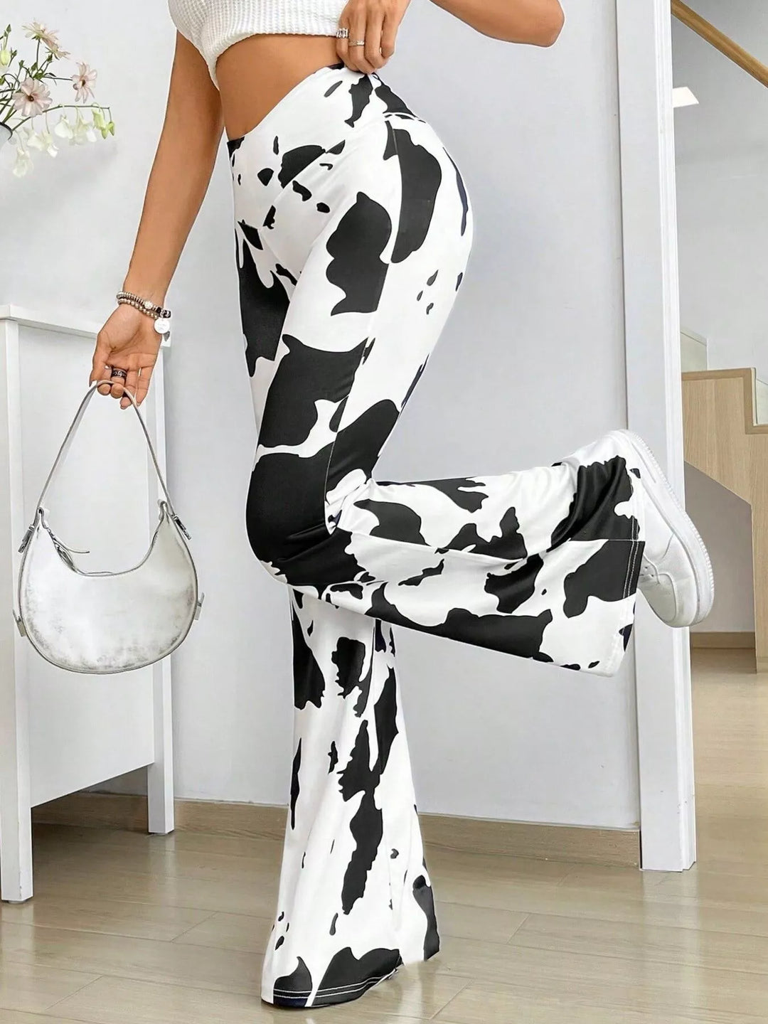 Cow print flare pants styled with a white top and bag, one leg lifted