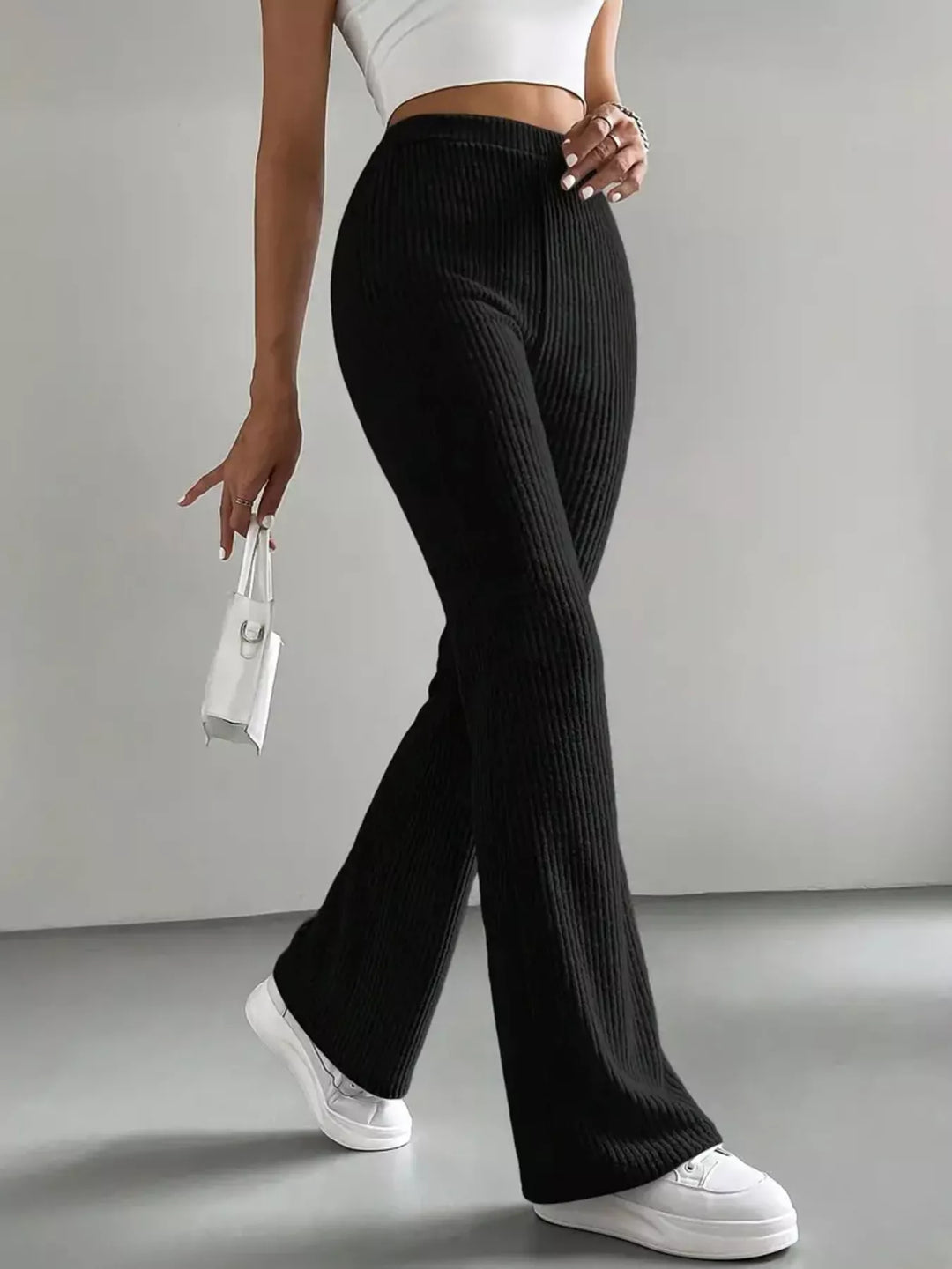 Black flare pants full length with a small white bag in hand