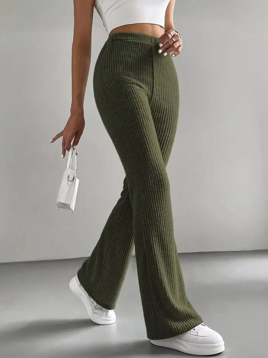 Women's flare pants in olive green, high waisted ribbed look, walking pose with white sneakers