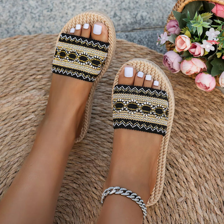 Pair of black woven slide sandals with patterned band, seen from above