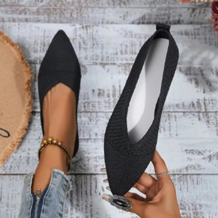 Black knit slip on flat held in hand to show the white insole