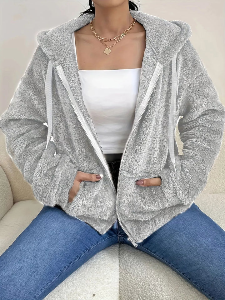 Light gray hooded zip up fleece jacket with drawstring hood over a white top and jeans
