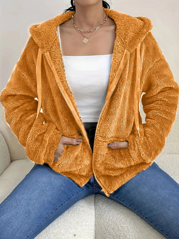 Orange hooded zip up fleece jacket with drawstring hood over a white top and jeans