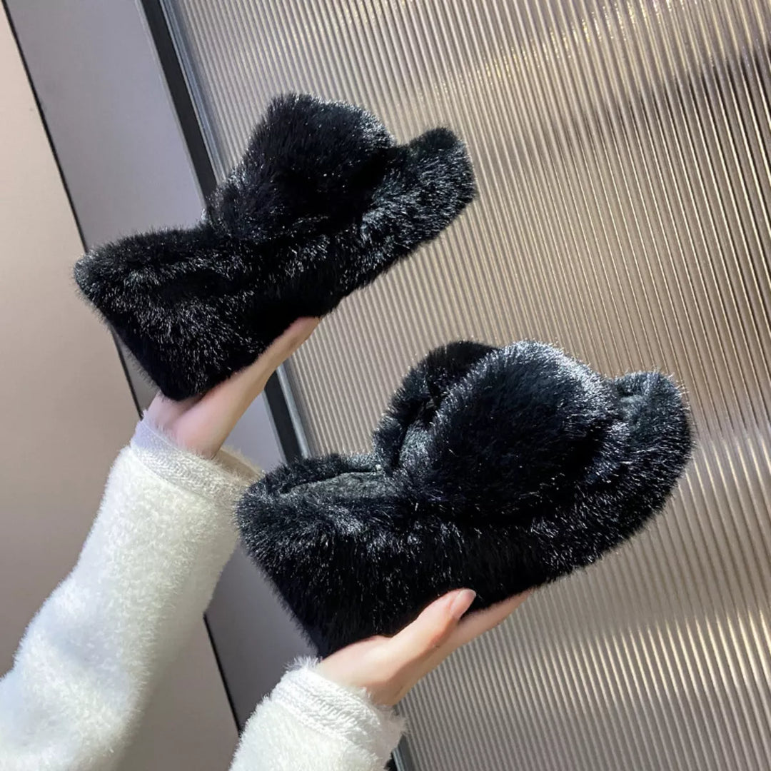 Black wedge platform slippers held in hand to show the crossed straps and thick sole