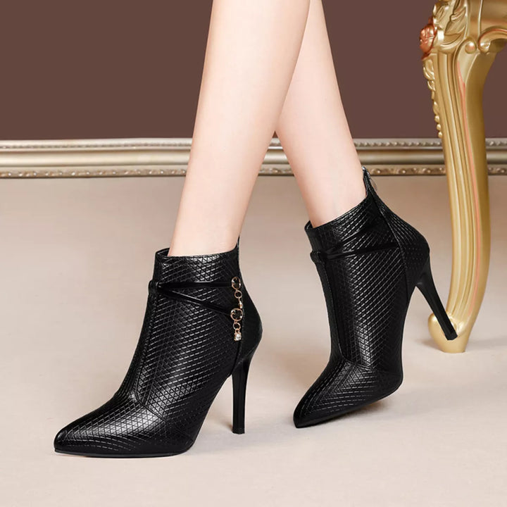 Black pointed toe cross strap heeled boots standing side by side near a gold chair leg