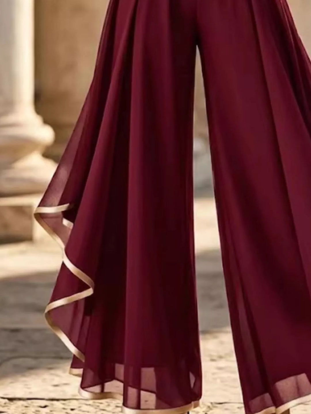 Close-up of the burgundy sheer overlay with gold trimmed asymmetric hem