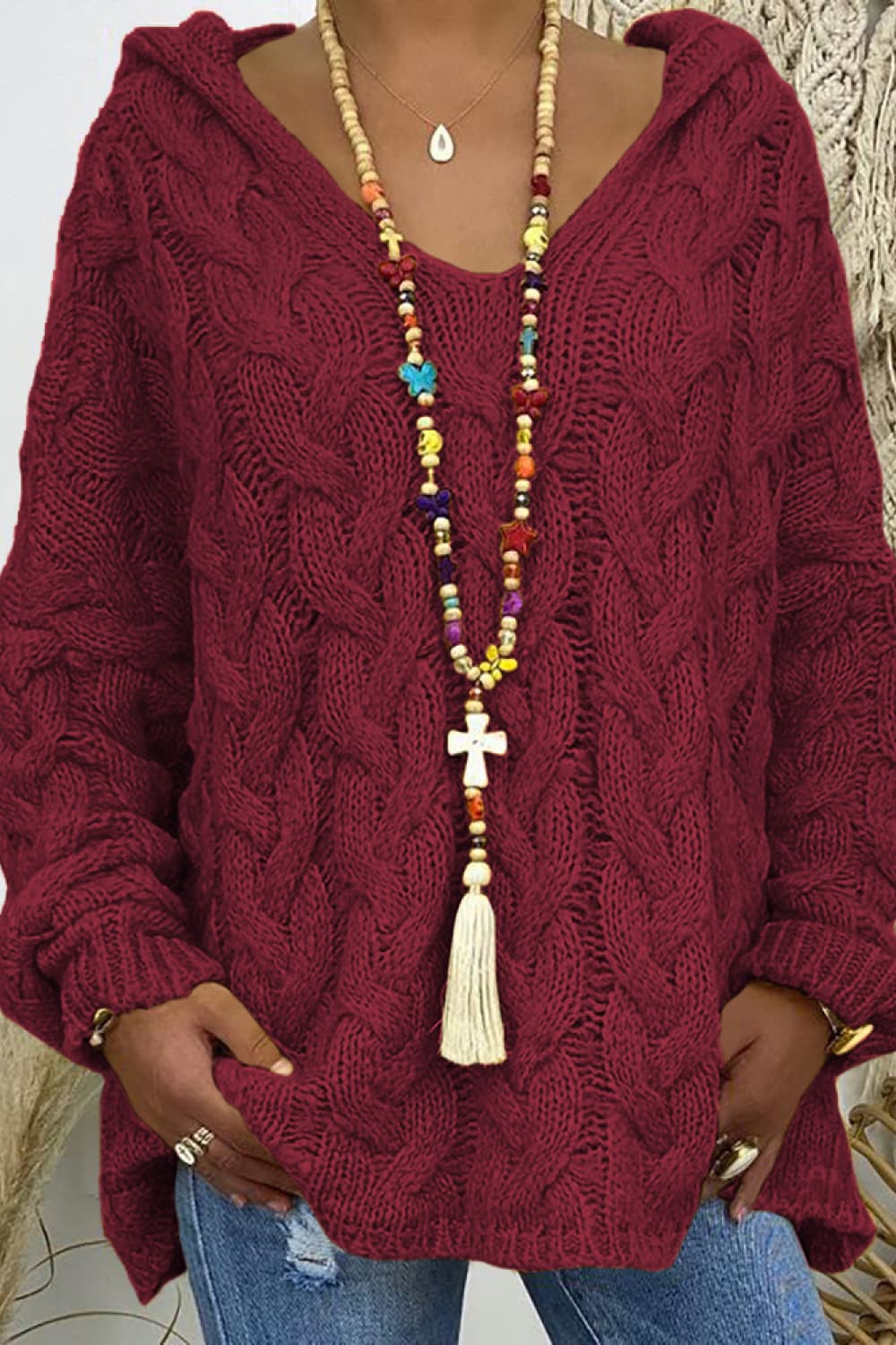 Close-up of the burgundy cable knit hooded sweater with V neck and long tassel necklace