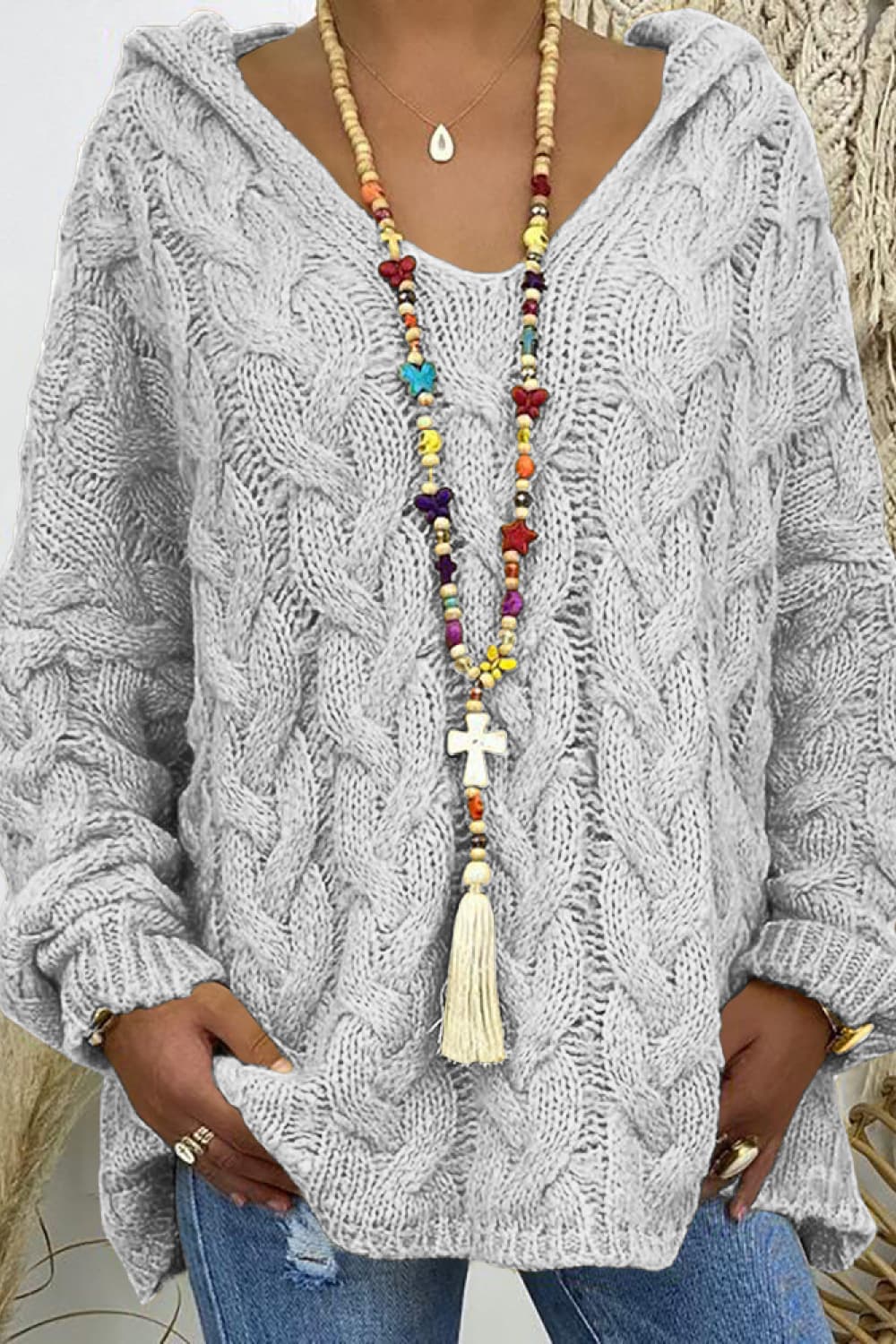 Light gray cable knit hooded sweater, close-up with V neck and beaded tassel necklace