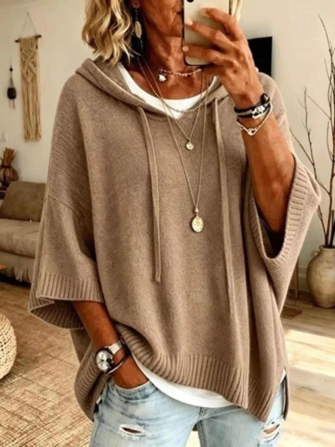 Taupe batwing sleeve hooded sweater, hand in jeans pocket and white tee layered below