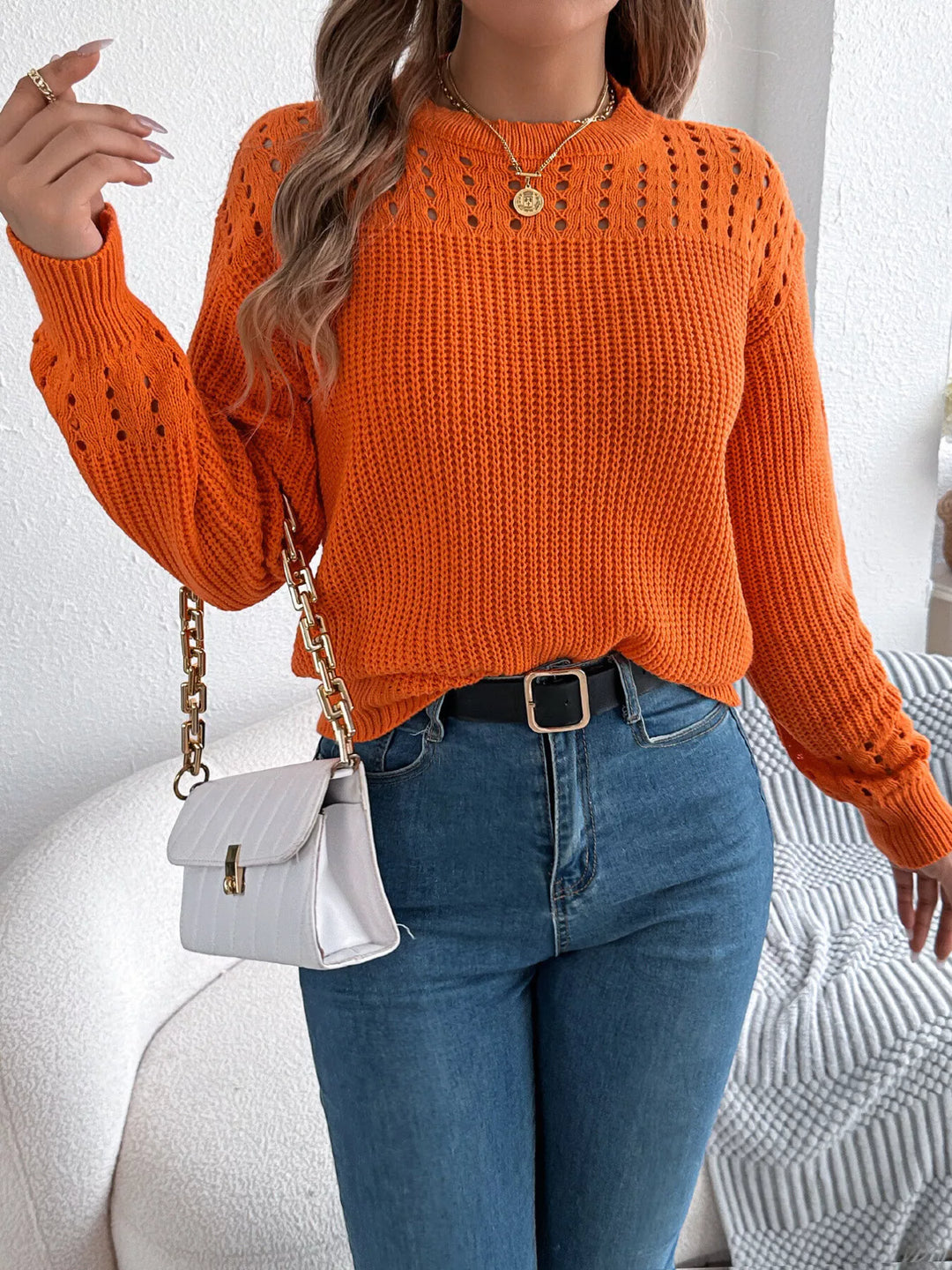 Orange knit sweater styled with a small white crossbody bag and jeans