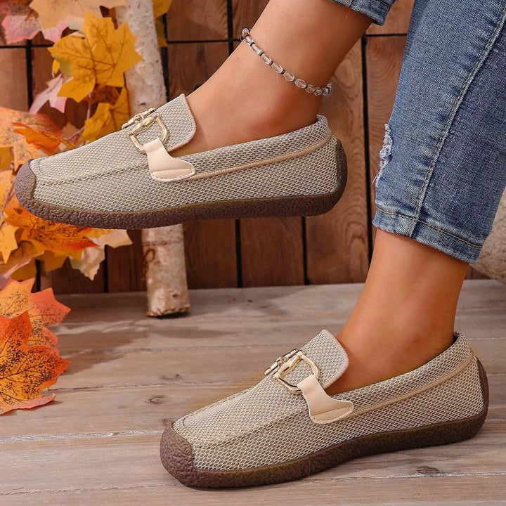 Pair of beige comfortable loafers with a buckle, fall leaves in the background