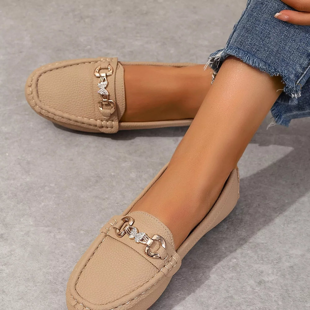Beige slip on moccasin loafer with a gold-tone buckle, top angle on a gray floor