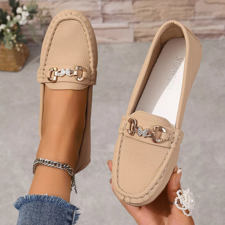 Hand holding a beige loafer to show the gold-tone buckle and white insole