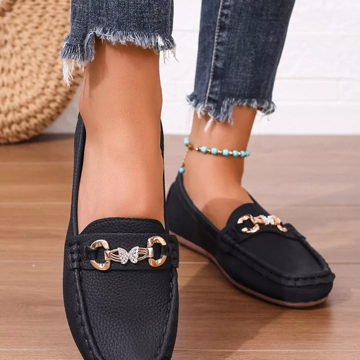 Front view of black slip on loafers with a gold-tone buckle and beaded anklet