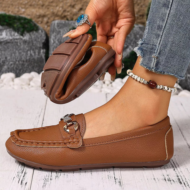 Cognac moccasin flat with a gold-tone buckle, one shoe lifted to show the sole