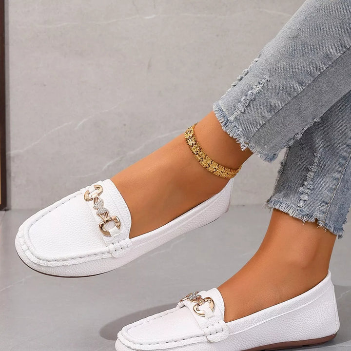 White slip on moccasin loafers with a gold-tone buckle, worn with frayed jeans