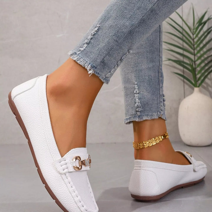 Side view of a white moccasin flat with a gold-tone buckle and gold anklet