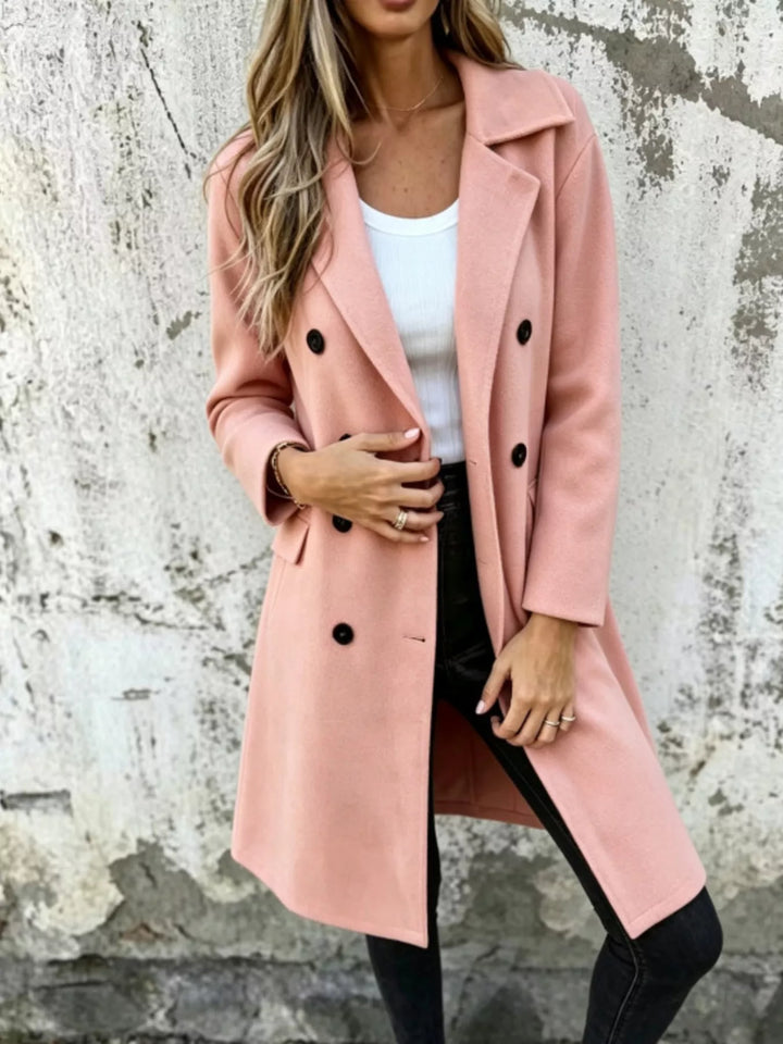 Pink knee length double breasted coat, standing against a textured wall