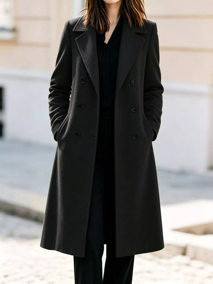 Black double breasted long coat with notch lapel, worn over a black outfit