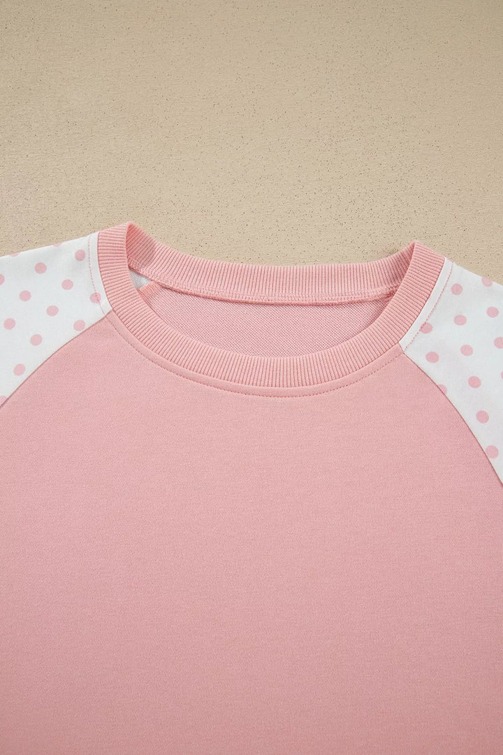 Close-up of the blush sweatshirt crew neckline and polka dot sleeve panels