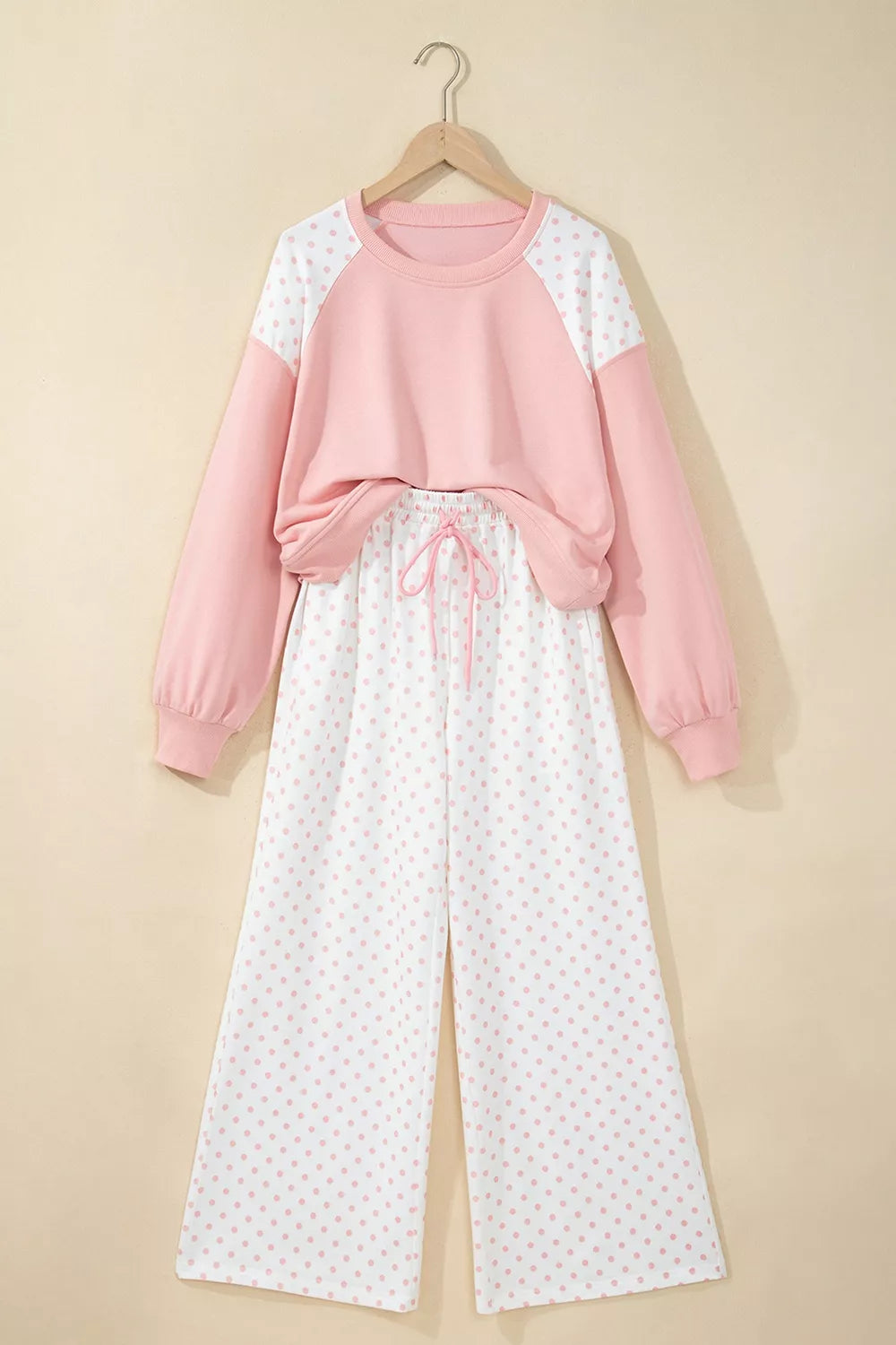 Blush cropped sweatshirt and polka dot pants hanging on a hanger