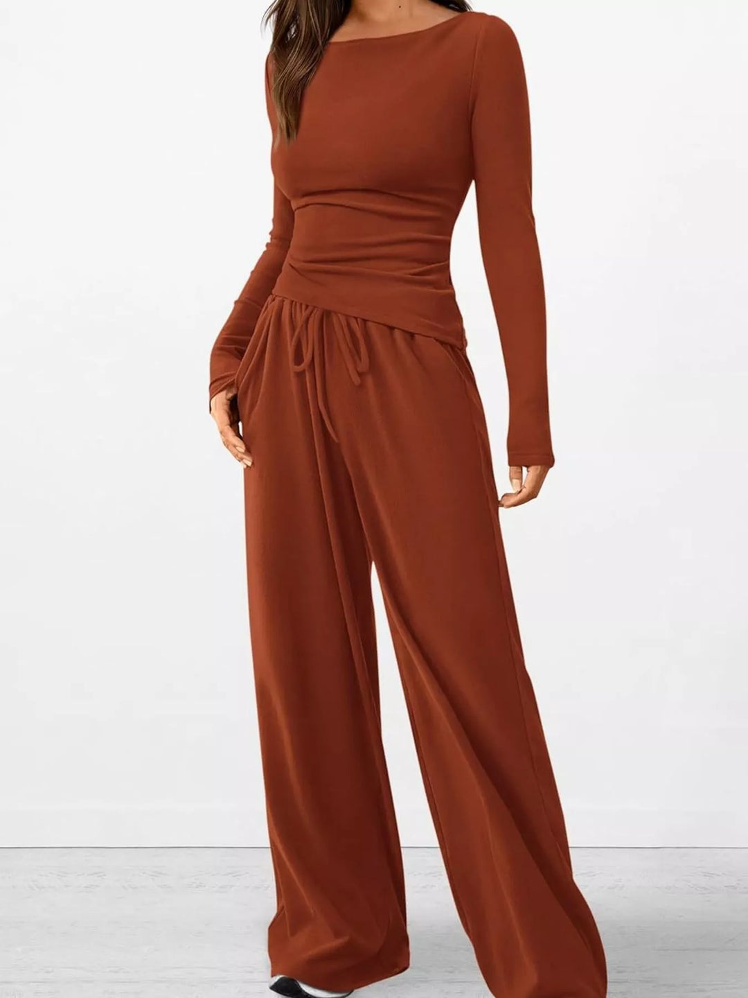 Rust ribbed knit lounge set with a ruched top, seated on the floor with sneakers