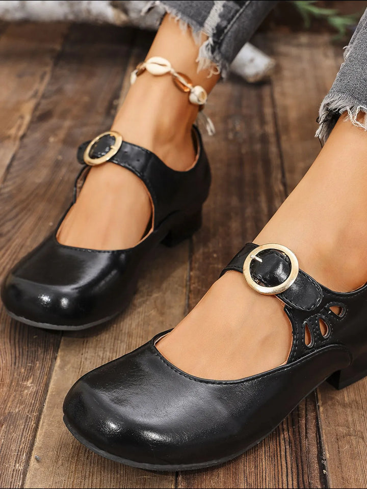 Black Mary Jane shoes with round toe and buckle strap on a wood floor