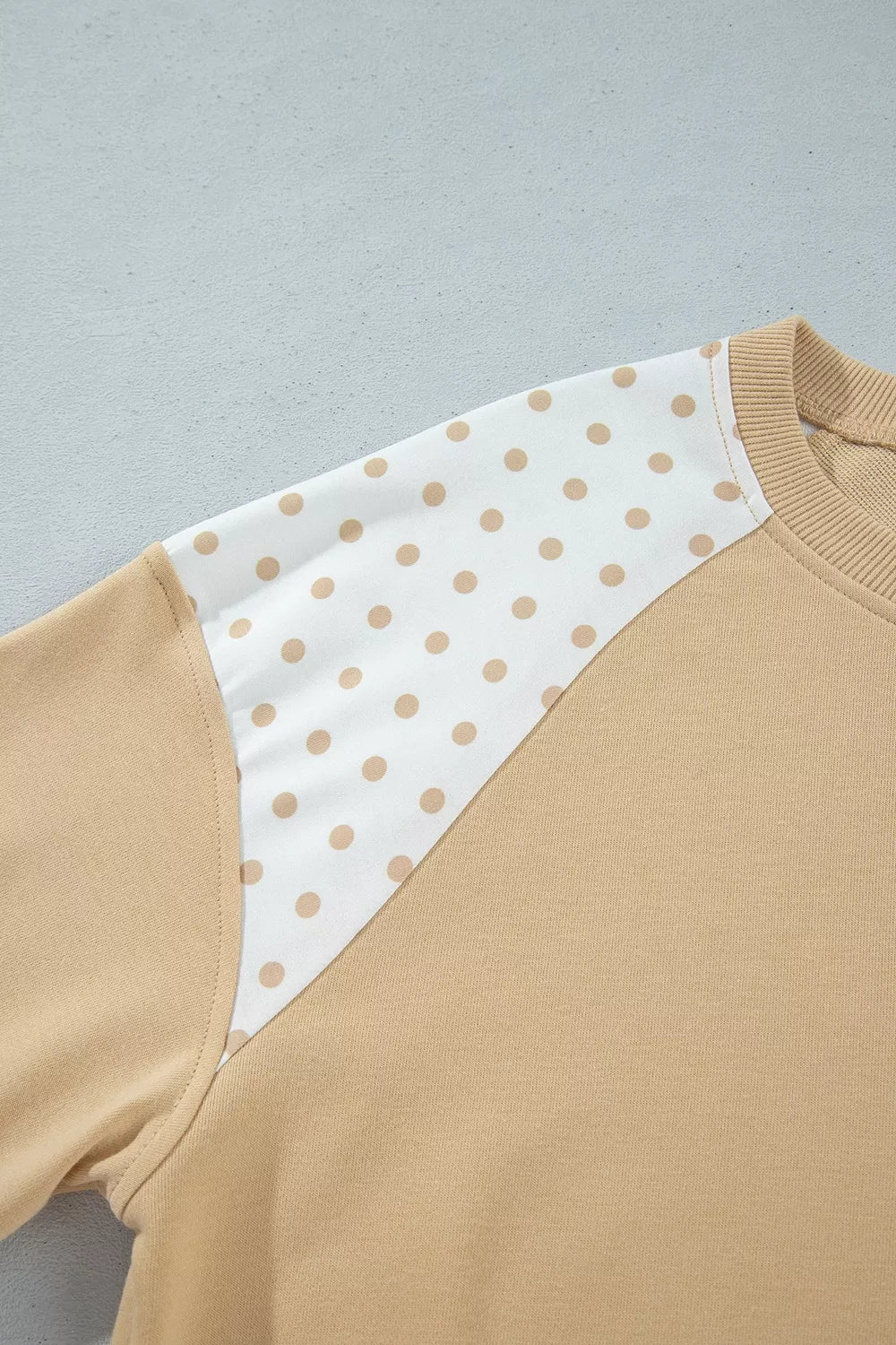 Raglan sleeve seam where tan fabric meets the polka dot panel