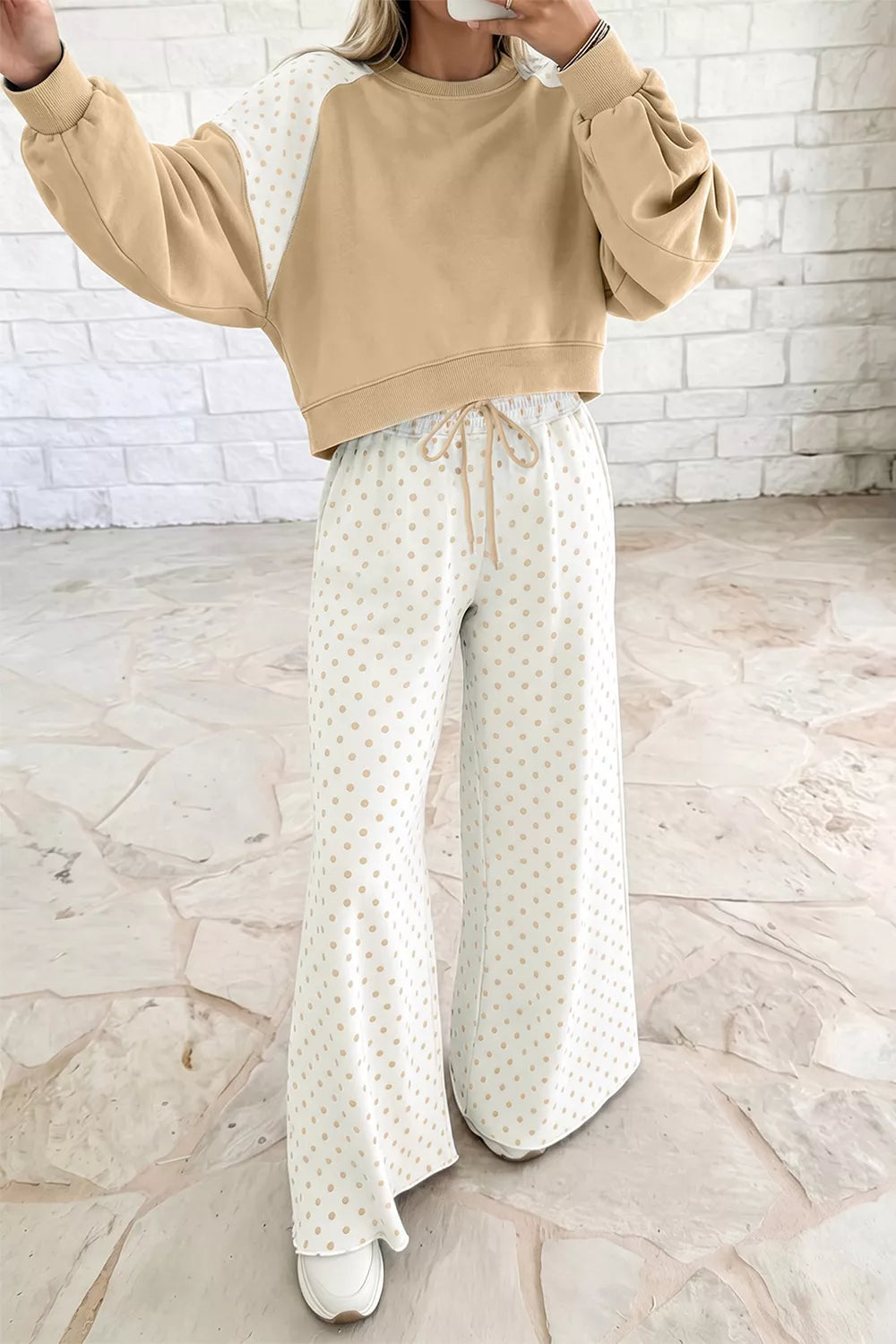 Tan cropped sweatshirt with raised arm, worn with polka dot pants on model