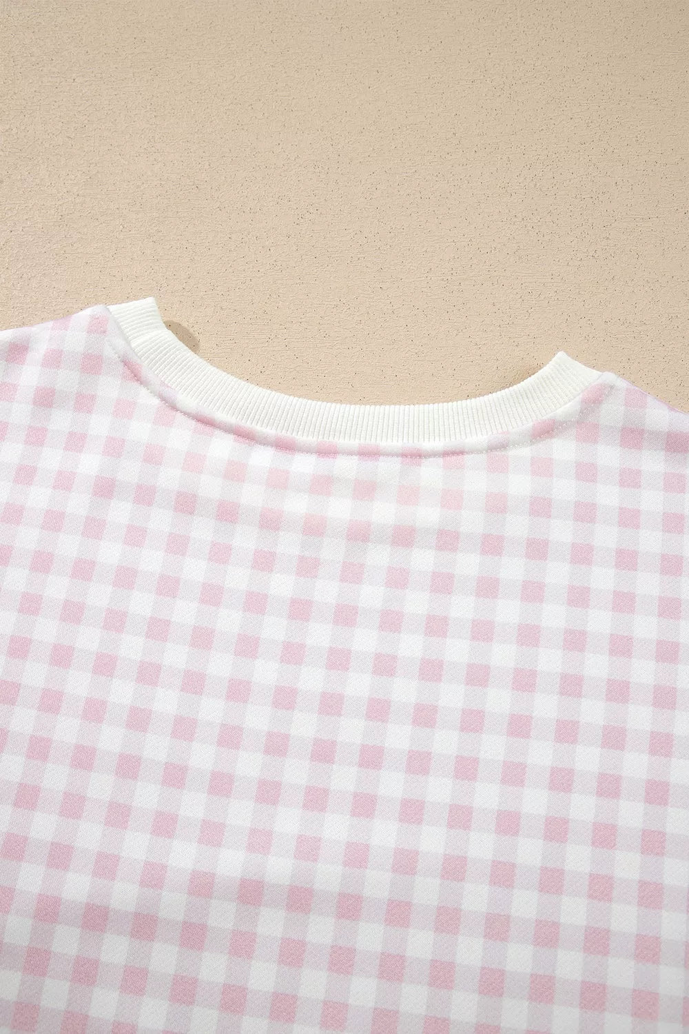 Neckline of the pink and white check sweatshirt laid flat