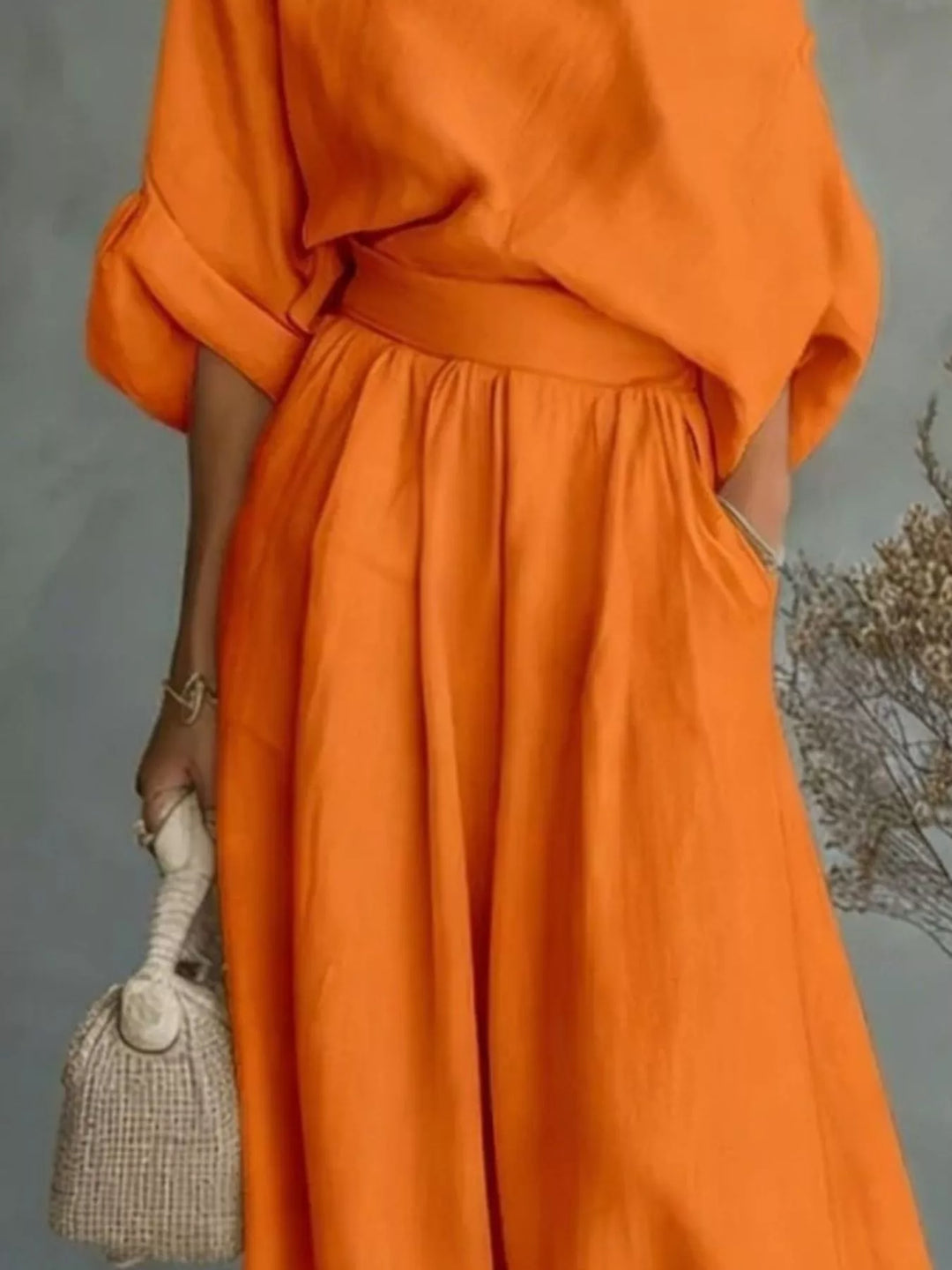 Orange wide leg maxi pants and one shoulder top, closer view with a woven bag