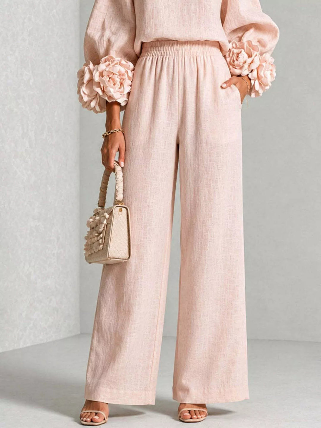 Blush pink wide leg pants and rose cuff top, angled pose with a handbag