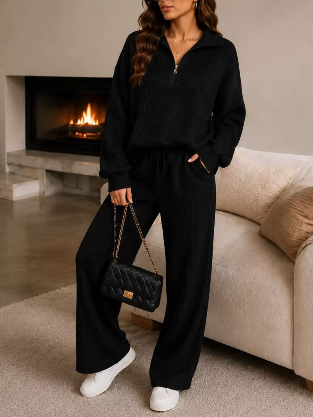 Black ribbed knit half zip pullover and wide leg pants, standing by a fireplace