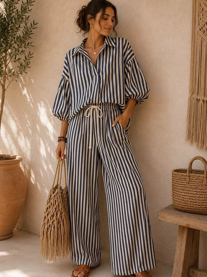 Black striped collared shirt and wide leg pants set, standing with a woven bag