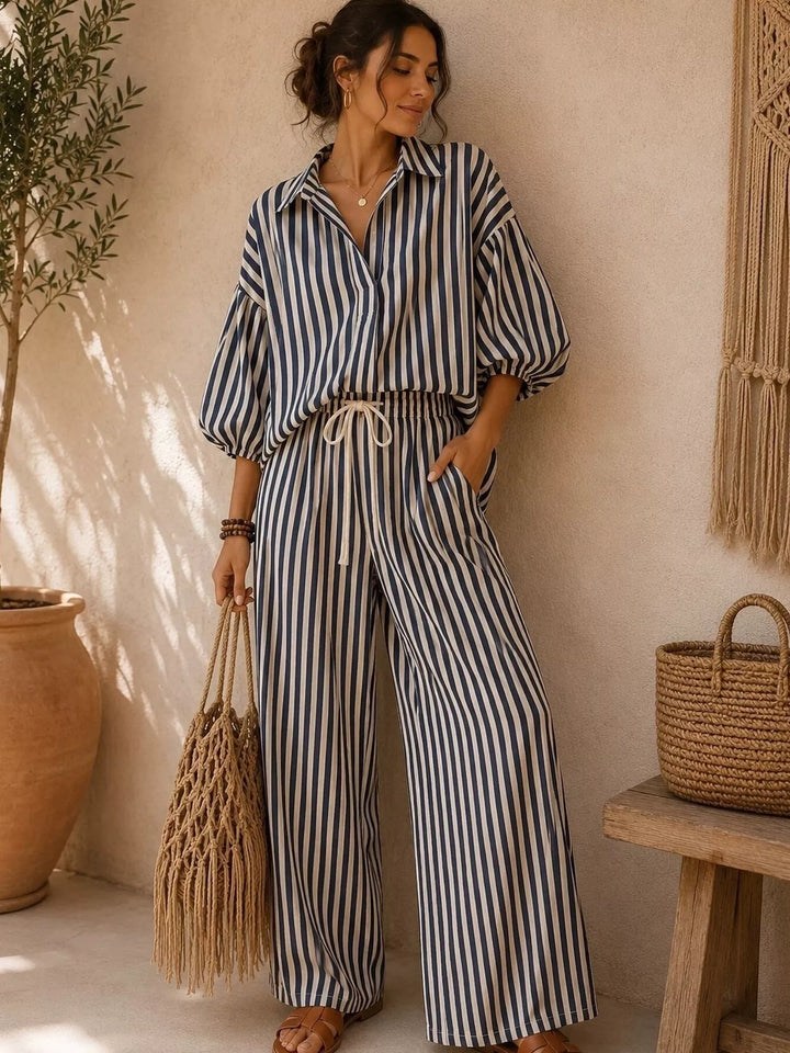 Black striped collared shirt and wide leg pants set, standing with a woven bag