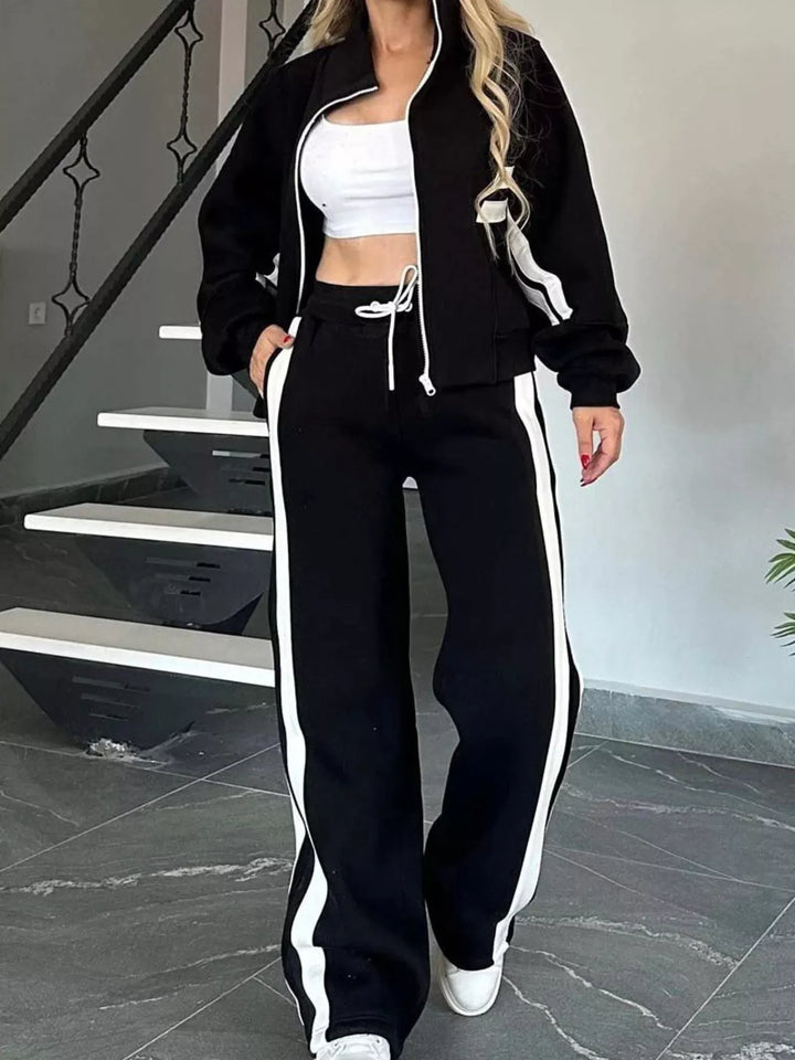 Women's black matching set, tracksuit zip up jacket and pants with side stripes, near stairs