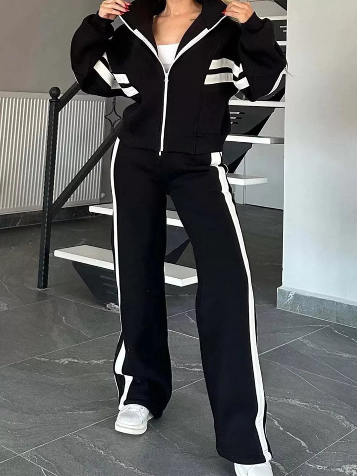 Black zip up tracksuit jacket and pants, hands holding the collar, white sneakers