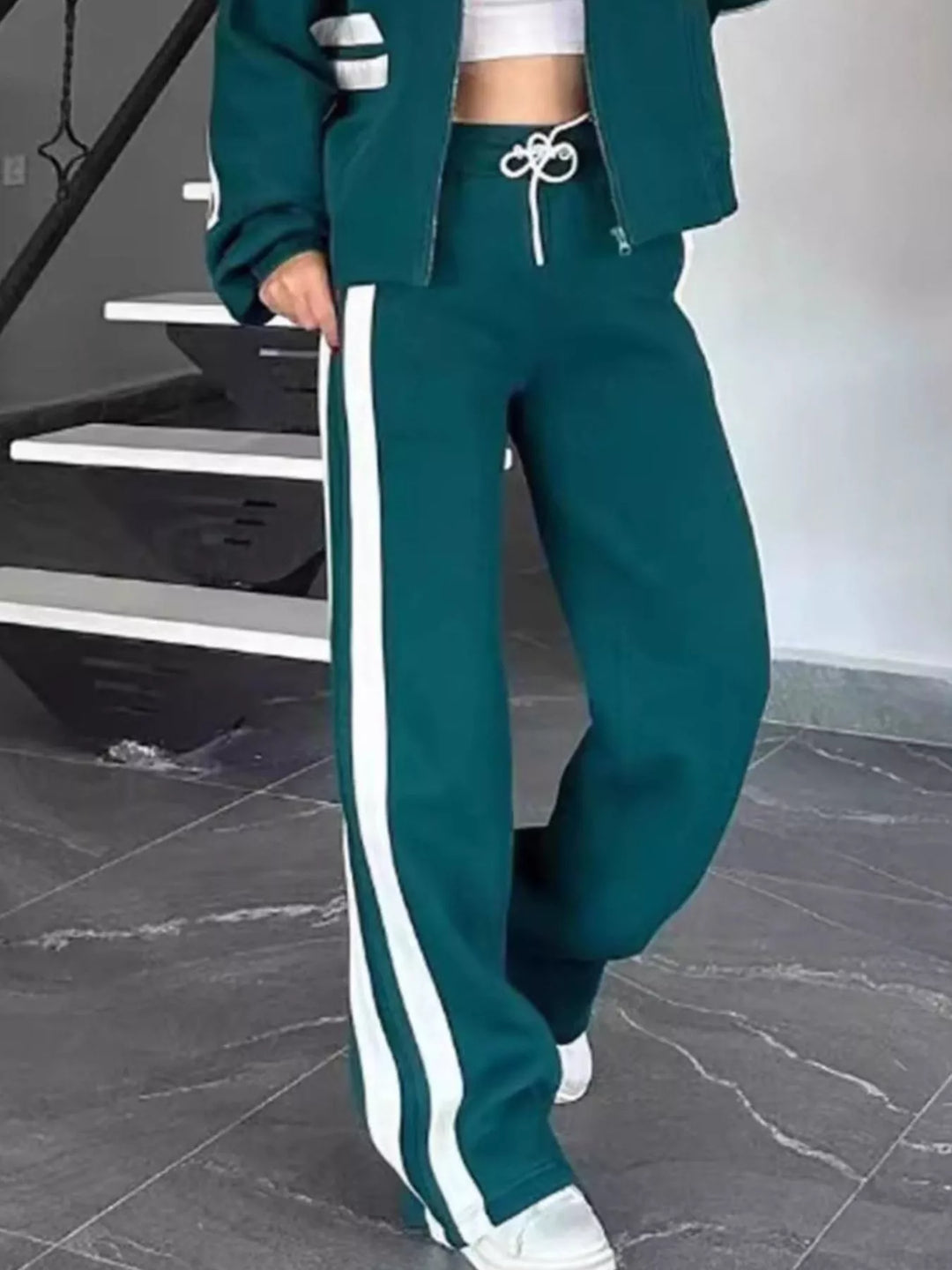 Teal tracksuit pants with white side stripe, stepping forward in sneakers