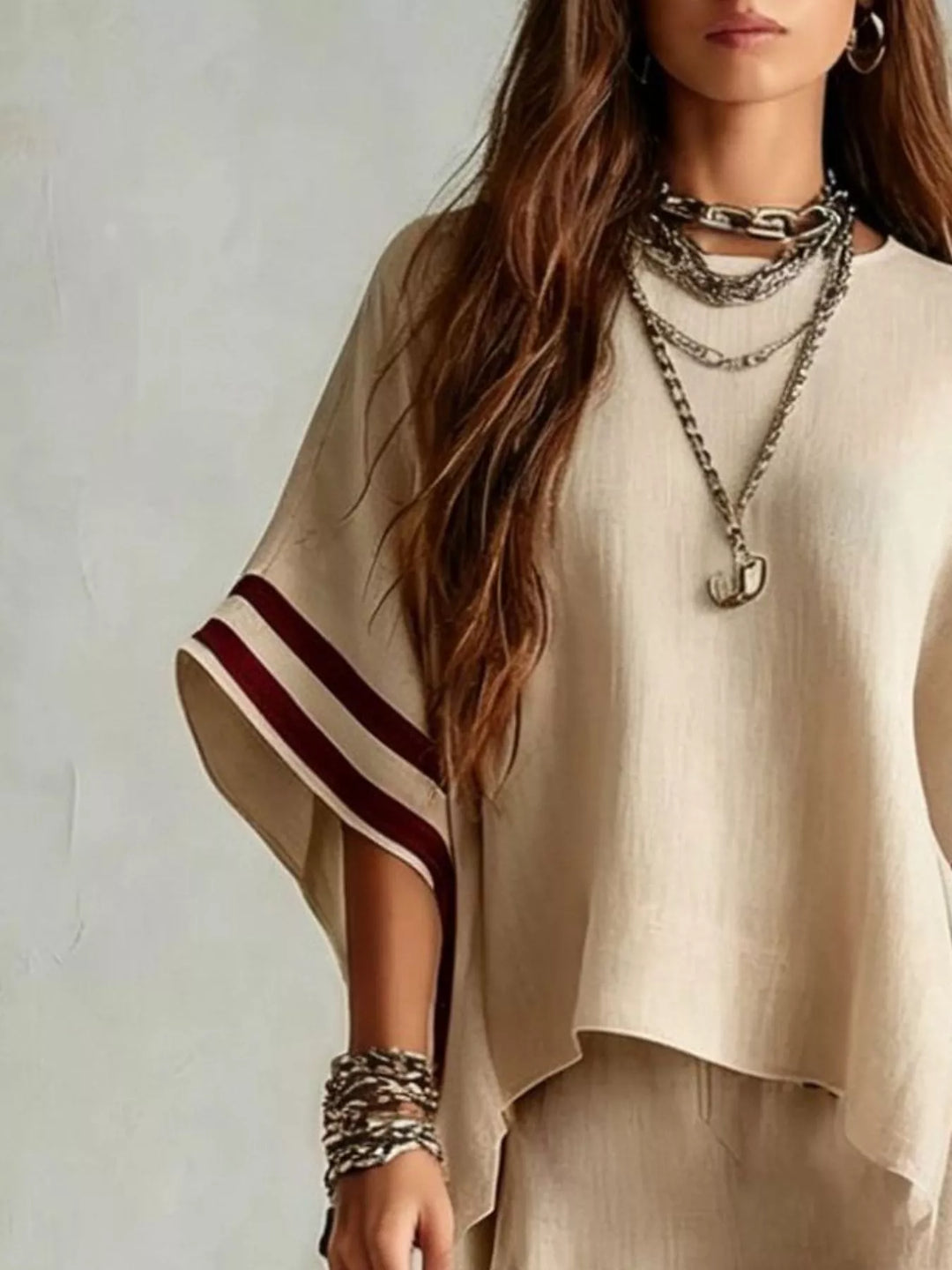Close-up of the beige wide sleeve top with burgundy striped cuffs and layered necklaces