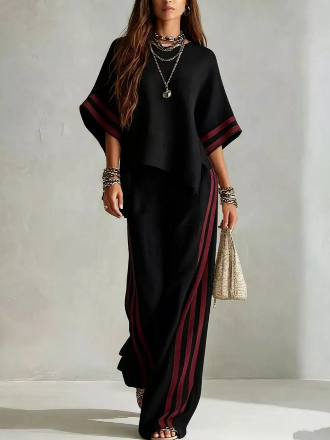Black wide sleeve top with burgundy striped pants, walking with a woven bag