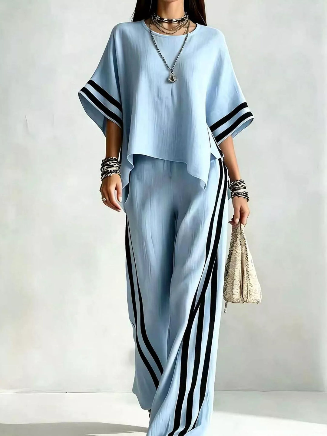 Light blue wide sleeve top and black striped pants set, standing with a bag